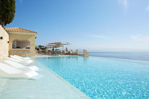 a swimming pool with white chairs and the ocean at Nido, Mar-Bella Collection in Agios Ioannis Peristeron