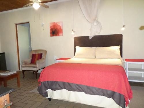 a bedroom with a bed with a red blanket and a chair at Geckos B&B and Self-catering in Coffee Bay