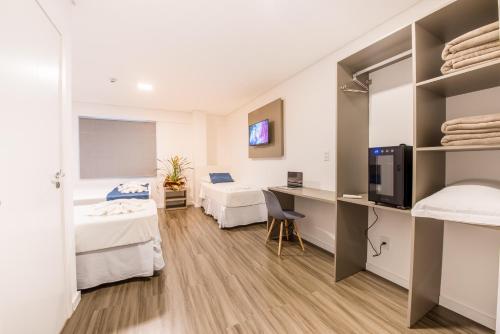 a room with two beds and a desk with a tv at Prime Hotel Ponta Porã in Ponta Porã