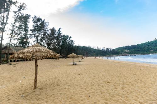 a beach with some straw umbrellas and the ocean at Quỳnh Viên Resort in Dương Luật