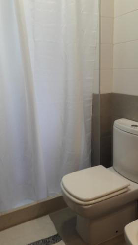 a bathroom with a toilet and a white shower curtain at Apart Altos del Virrey in Colonia del Sacramento