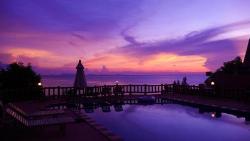 a sunset over a swimming pool with an umbrella at Zama Resort Koh Phangan in Haad Chao Phao