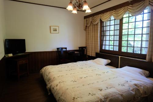 a bedroom with a bed and a tv and windows at Appikogen Pension Mutti in Hachimantai