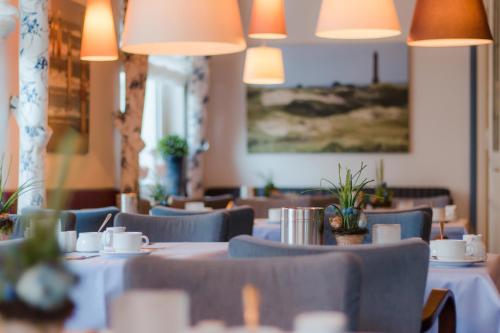 um restaurante com mesas brancas, cadeiras e luzes em Inselhotel Bruns em Norderney