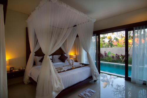 a bedroom with a canopy bed and a swimming pool at The Awan Villas - CHSE Certified in Seminyak