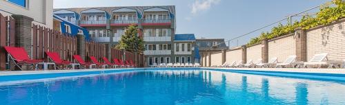a large swimming pool with red chairs in front of a building at Hotel Topol in Anapa