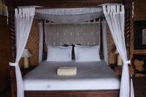 una camera con letto a baldacchino con lenzuola e cuscini bianchi di Oka 7 Bungalow a Nusa Lembongan