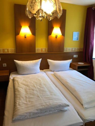 1 Schlafzimmer mit 2 Betten mit weißer Bettwäsche und einem Kronleuchter in der Unterkunft Hotel Südheide in Hermannsburg
