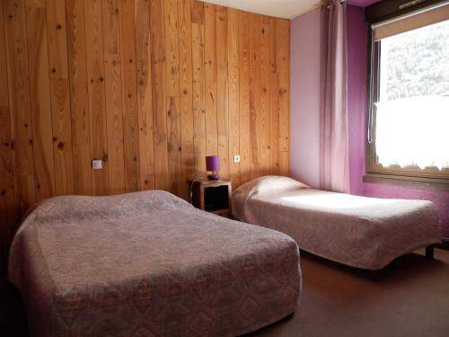 two beds in a room with a window and wooden walls at Hotel La Gare in LʼArgentière-la-Bessée