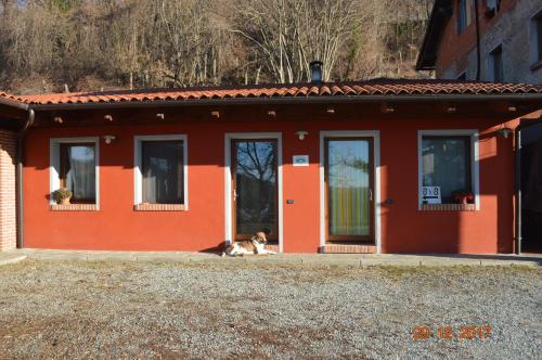 a dog laying in front of a red house at B&B Cascina Bedria in Ivrea