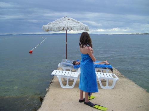a woman in a blue dress standing on a dock with an umbrella at Apartmani Luka in Vir