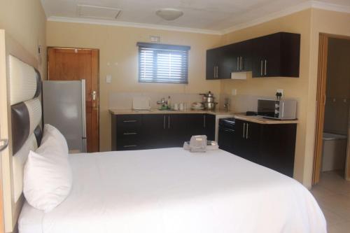 a bedroom with a white bed and a kitchen at Mbopha Guest House in Ulundi