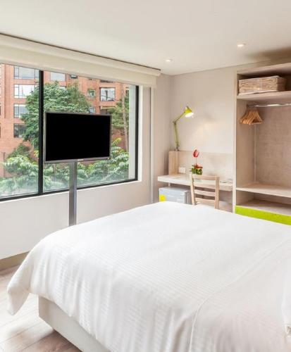 a white bedroom with a large bed and a flat screen tv at Mika Suites in Bogotá