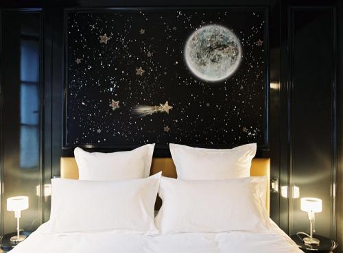 a bed with white pillows and a poster of the moon at Hôtel du Petit Moulin, Haute Couture hotel by Lacroix in Paris