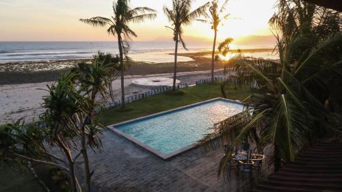 a swimming pool next to the beach at sunset at The Tree House Sumbawa in Huu