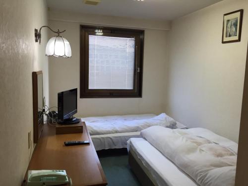 um quarto com 2 camas e uma secretária com uma televisão em Aoi Business Hotel em Fukuyama