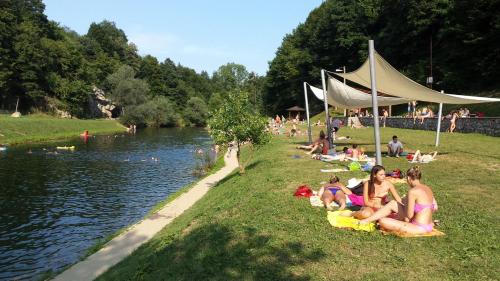 a group of people sitting on the grass near a river at Apartments Strmac in Slunj