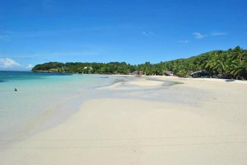 a white beach with trees and the ocean at Chekesh Casa in Siquijor