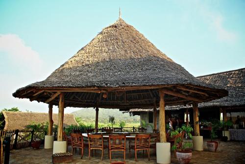 a restaurant with a straw roof and tables and chairs at Manyatta Camp in Voi