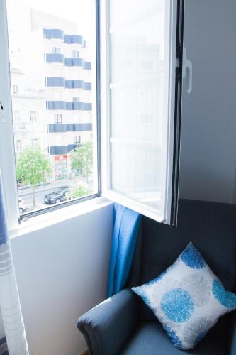 a blue chair sitting under a window with a pillow at Soldouro Guesthouse in Aveiro