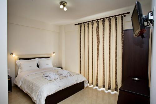 een slaapkamer met een bed met witte lakens en een televisie bij Rg Status Hotel in Paralia Katerinis