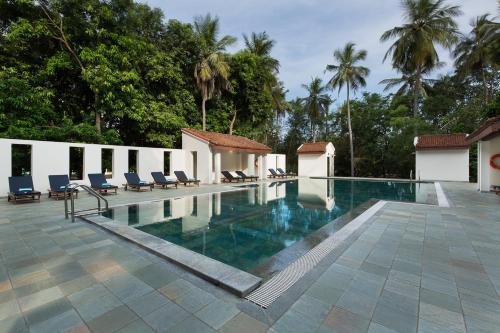 a swimming pool in a resort with chairs and trees at Mantra Koodam Kumbakonam - a CGH Earth Experience in Kumbakonam