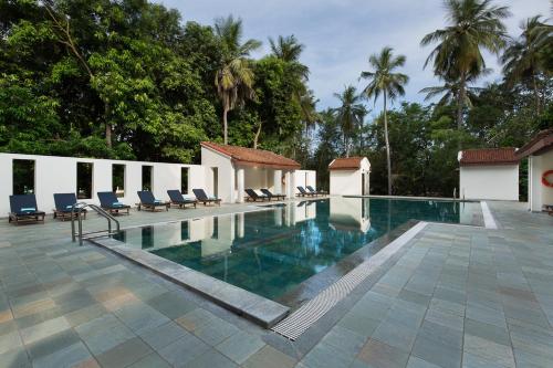 einen Pool in einem Resort mit Stühlen und Bäumen in der Unterkunft Mantra Koodam Kumbakonam-CGH Earth in Kumbakonam