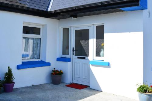 een wit huis met een blauwe deur en ramen bij Cottage 312 - Ballyconneely in Ballyconneely
