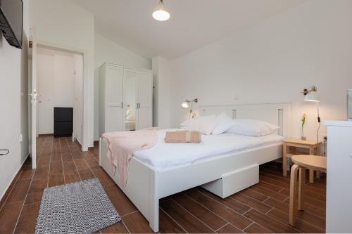 a white bedroom with a white bed and a table at Kvasina Apartments in Zadvarje