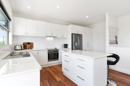 a white kitchen with white cabinets and a refrigerator at Rosewater Townhouses Dromana in Dromana