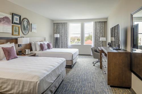 a hotel room with two beds and a desk at Hotel Madison & Shenandoah Conference Ctr. in Harrisonburg