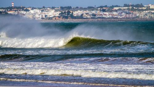 a large wave in the ocean with a city in the background at Casas Novas Guesthouse - Adults Only in Lagos