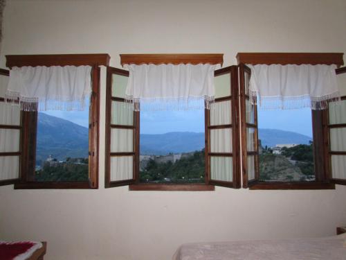 four windows in a bedroom with mountains in the background at Guest House Salaria in Gjirokastër