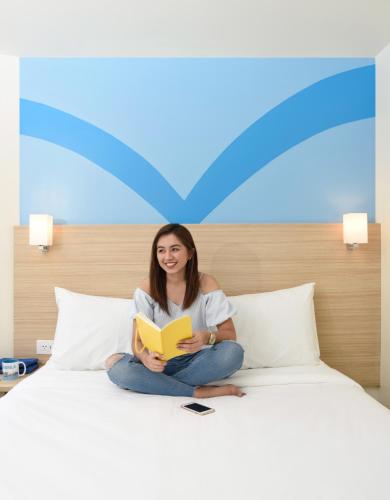 a woman sitting on a bed reading a book at Hop Inn Hotel Alabang Manila in Manila