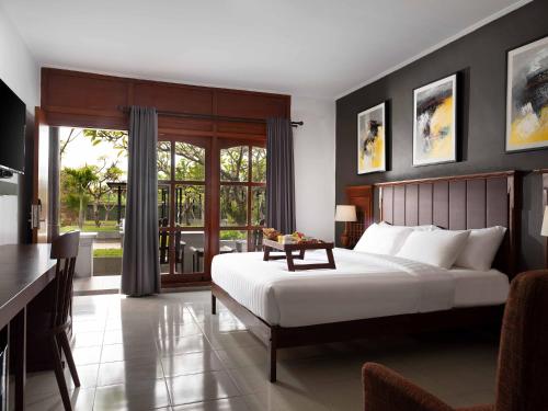 a bedroom with a white bed and a desk and a window at Brits Resort Lovina in Lovina