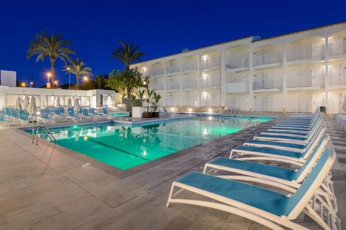 a swimming pool with lounge chairs in front of a hotel at Hotel Vibra Cala Tarida-3SUP in Cala Tarida