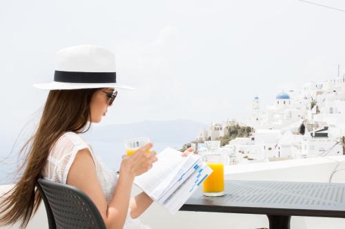 una mujer con sombrero sentada en una mesa leyendo un periódico en Agave Santorini Design Boutique Hotel, en Imerovigli