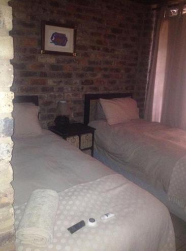a bedroom with two beds and a brick wall at Tranquillity Day Spa & Lodge in Baviaanspoort