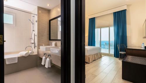 a bathroom with a tub and a sink and a bed at Radisson Blu Resort, Fujairah in Dibba