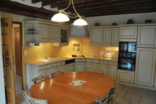 una cocina con mesa de madera y una cocina con armarios blancos. en Gîte Les aurégats, en Maligny