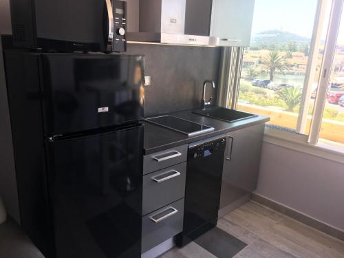 La cuisine est équipée d'un réfrigérateur noir et d'un évier. dans l'établissement Village Naturiste Agde, au Cap d'Agde