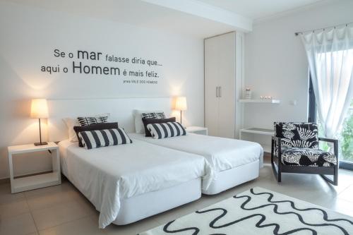 a white bedroom with two beds and a chair at Hotel Alcatruz in Aljezur