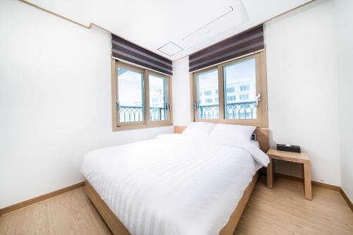 a white bedroom with a large bed and windows at Hotel Run in Seogwipo
