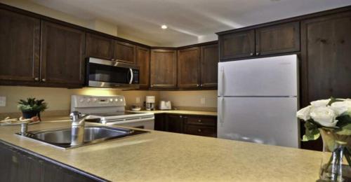 a kitchen with a sink and a white refrigerator at Aiglon by Rendez-Vous Mont-Tremblant in Mont-Tremblant