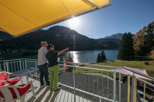 a man and woman standing on a deck looking at a lake at Hotel Seebüel in Davos