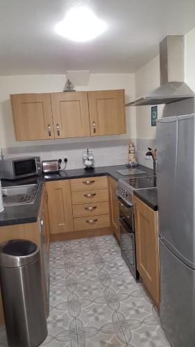 La cuisine est équipée d'armoires en bois et d'un réfrigérateur en acier inoxydable. dans l'établissement Chinwin Cottage, à Weymouth