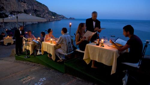 a group of people sitting at tables near the ocean at Villa Corallium in Praiano
