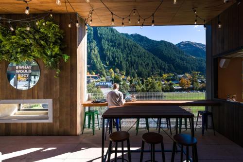 a man sitting at a table in a bar with a view at JUCY Snooze Queenstown in Queenstown