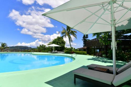 a swimming pool with a white umbrella and a chair at Coco Garden Resort Okinawa in Uruma