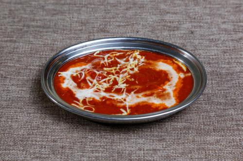 a metal bowl of sauce with cheese on a table at The Colonial Manek Manor By SAH in Mount Ābu